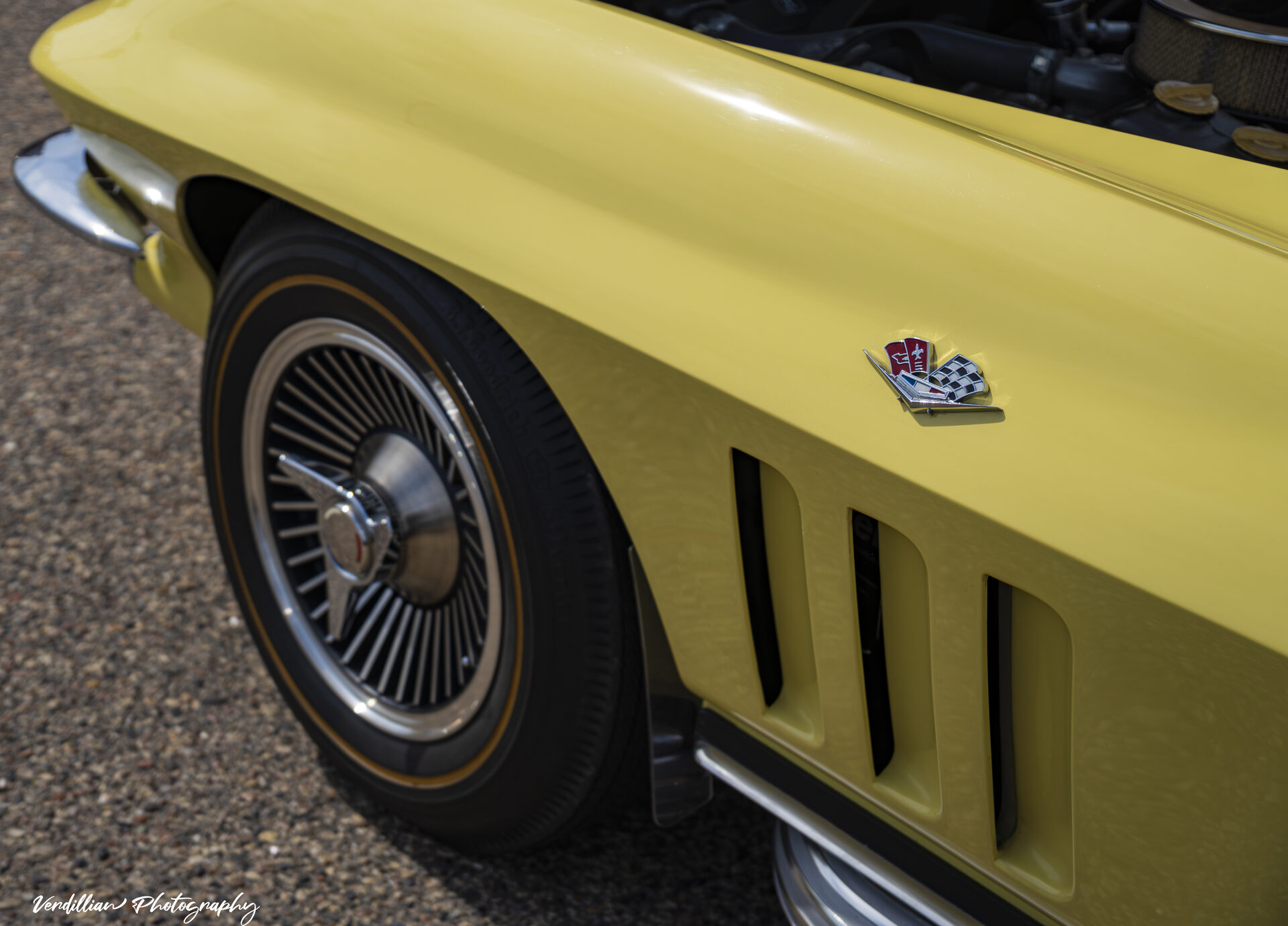 Close-up of a classic yellow Corvette's front fender badge and wheel